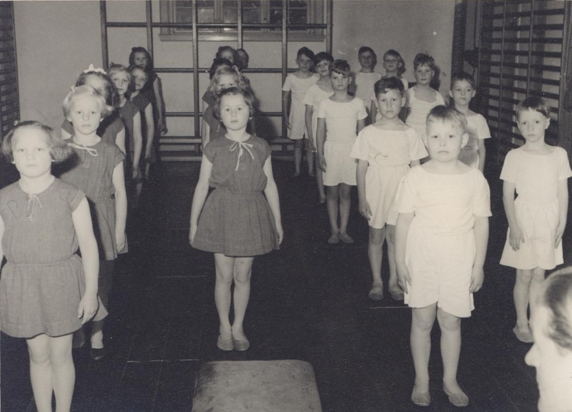 1950 Både drenge og piger på Kastelsvej linet op i den lille gymnastiksal til en gang arme bøj, arme stræk. Nødvendige øvelser, yndet af lærere, knap så meget af børnene.