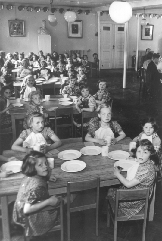 1950 Alle måltider omkring 1950 var henlagt til spisesalen. Pigerne sidder til venstre, drengene til højre med lærerne i midten. På væggene hænger billeder af danske konger i guldramme med krone. Der er tillige 3 buster, Frederik VI, P. A. Castberg og Rasmus Malling Hansen. Hele vejen rundt hænger de gamle tintallerkener.
