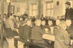 1907 Piger og drenge sidder hver for sig, når måltiderne skal indtages. Endnu i 1907 spiser og drikker man af tintallerkener og tinkrus. Lærerne sidder med til bords for at opretholde ro og orden.