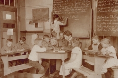 1916 En af skolens yngre lærere, Oskar Alberts, underviser i regning. Bemærk datidens skolepult med bænk foran. Ved denne kunne eleverne undervises uden at blive distraheret af andre ting.