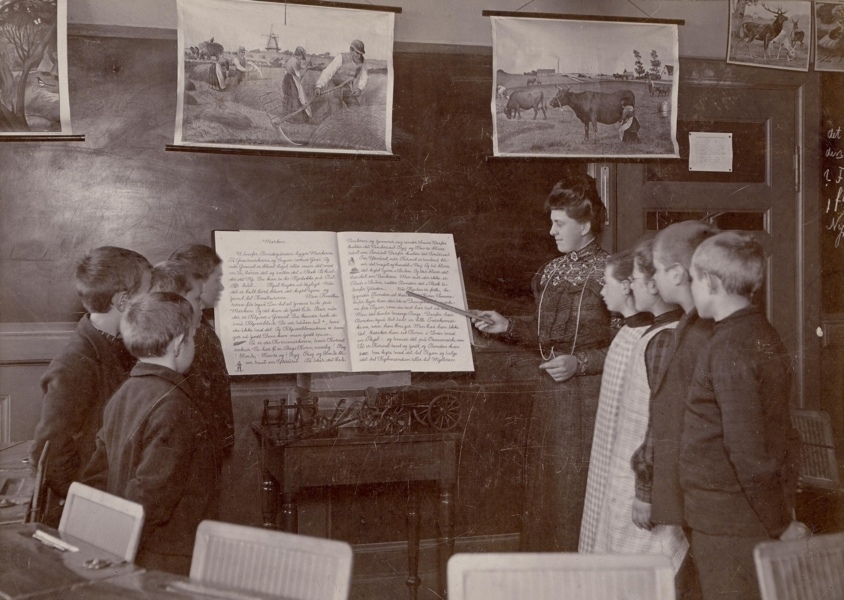 1907 Korlæsning efter Korlæsebog. Korlæsning i Fredericia med lærerinden som dirigent. Efter de ophængte anskuelsestavler at dømme, er emnet livet på landet
