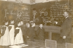 1907 Korlæsning efter Mund-Haandsystem. Indøvelse af MHS kunne også ske ved korlæsning. Det kan ikke have været helt nemt for eleverne, både at følge det skrevne ord på tavlen og lærerens mund og hånd