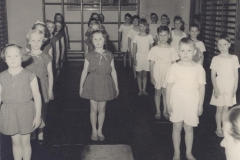 1950 Både drenge og piger på Kastelsvej linet op i den lille gymnastiksal til en gang arme bøj, arme stræk. Nødvendige øvelser, yndet af lærere, knap så meget af børnene.
