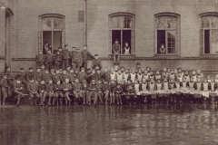 1909 Den nyudnævnte forstander, Anders Hansen, har samlet alle eleverne i den regnvåde gård. At en dreng har fået lov til at sidde i vindueskarmen, er vist ikke helt efter Anders Hansens regler.